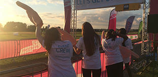 Volunteers at the finish line, standing behind pink banners, cheering participants on as they complete their Race for Life 10k event.