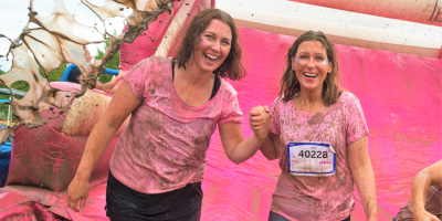Two women smiling holding hands in a Pretty Muddy event